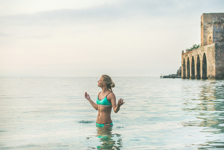 Young beautiful slavian woman tourist wearing turquoise bikini relaxing in sea at beach near ancient fortress wall and shipyard in city center of Alanya, Mediterranean Turkeyの写真素材