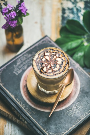 Latte coffee with chocolate sauce pattern in tall glass over rustic table with books background, selective focusの写真素材