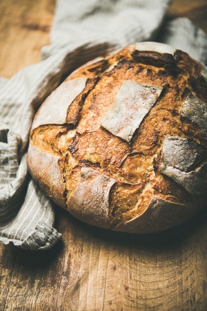 Freshly baked sourdough wheat bread loaf over linen napkin and rustic wooden table background, selective focus, vertical compositionの写真素材
