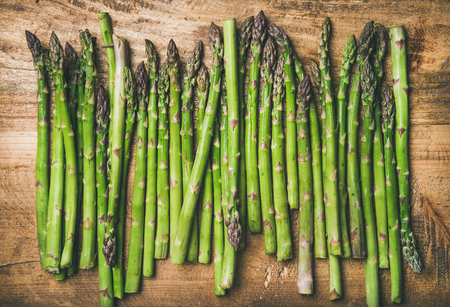Seasonal harvest produce . Flat-lay of raw uncooked green asparagus in row over rustic wooden background, top view. Local market food conceptの写真素材