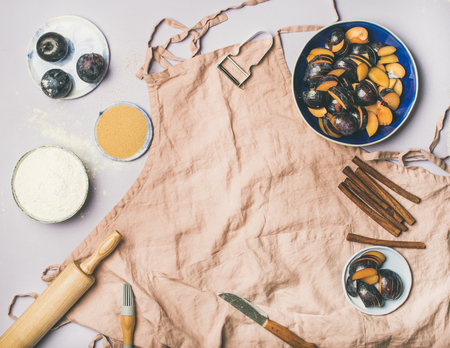 Baking ingredients and tools. Flat-lay of dusty pink linen apron, kitchen utensils, flour, sugar, fruit and spices over pastel lilac background, top view, copy spaceの写真素材