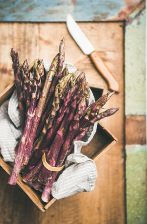 Seasonal harvest produce. Fresh raw uncooked purple asparagus over rustic wooden tray background, selective focus, vertical composition. Local market food conceptの写真素材