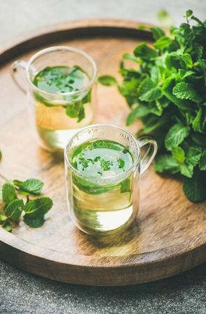 Hot herbal mint tea drink in glass mugs over wooden tray with fresh garden mint leaves, selective focus, vertical compositionの写真素材