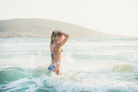 Young beautiful blond woman tourist in swimsuit standing and relaxing in wavy waters of Mediterranean sea in Prasonisi cape, Rhodes, Greeceの写真素材