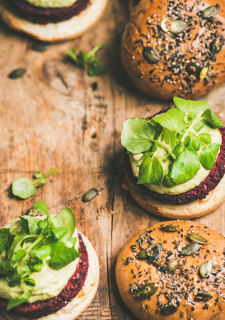 Healthy vegan burgers with quinoa beetroot patties, avocado cream and green sprouts over wooden board background, copy space. Vegetarian, clean eating foodの写真素材
