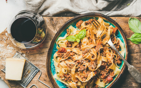 Italian traditional pasta dinner. Flat-lay of Tagliatelle bolognese with minced meat, tomato sauce and grated parmesan cheese and glass of red wine over rustic wooden board background, top viewの写真素材
