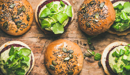 Flat-lay of healthy vegan burgers with quinoa beetroot patties, avocado cream and green sprouts over wooden background, top view, copy space, horizontal composition. Vegetarian, alcaline diet foodの写真素材