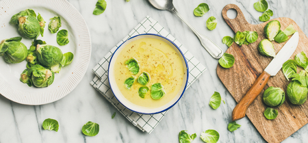 Flat-lay of seasonal brussels sprouts vegetable cream soup in bowl and fresh green brussel sprouts over marble background, top view, wide composition. Vegan, vegetarian, healthy, dieting food conceptの写真素材