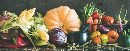Fall vegetarian food ingredients. Assortment of various Autumn vegetables for healthy cooking over rustic cupboard, dark wall background, copy space, wide composition. Local market organic produceの写真素材