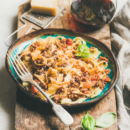 Italian traditional pasta dinner. Tagliatelle bolognese with minced meat, tomato sauce and parmesan cheese and glass of red wine over rustic wooden board, selective focus, square cropの写真素材