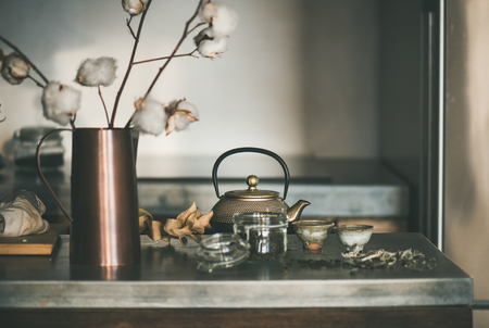 Tea ceremony. Golden iron teapot and japanese ceramic cups full of green tea drink on grey concrete kitchen counter, selective focus. Cold winter morning at homeの写真素材