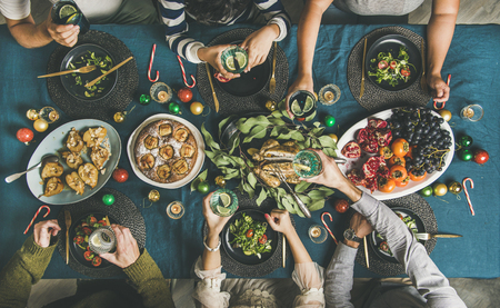 Company of friends of different ages gathering for Christmas or New Year party dinner at festive table. Flat-lay of human hands holding glasses with drinks, feasting and celebrating holiday, top viewの写真素材
