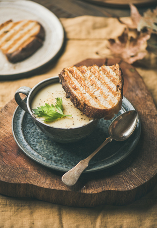 Autumn, Winter home dinner. Fall warming celery cream soup in cup and toast over yellow linen tablecloth. Comfort food, vegan, vegetarian, healthy and slow food conceptの写真素材