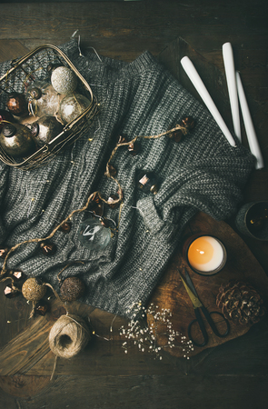 Christmas, New Year holiday festive mood. Flat-lay of grey woolen sweater, candle, led garland and vintage stylish Christrmas decoration toys in box over wood rustic table background, top viewの写真素材