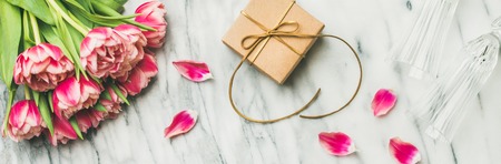 Valentines day holiday background. Flat-lay of pink tulips bouquet, champaign glasses and gift box with ribbon over white marble table, top view. Lovers or Womens day greeting cardの写真素材