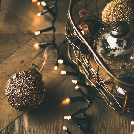 Christmas or New Year background. Vintage Christmas tree golden toy decoration balls in box and light garland over rustic wooden background, selective focus, copy space, square cropの写真素材
