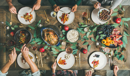 Traditional Christmas, New Year holiday celebration. Flat-lay of friends or family eating various food at festive table with turkey or chicken, vegetables, mushroom sauce, fruit, top viewの写真素材