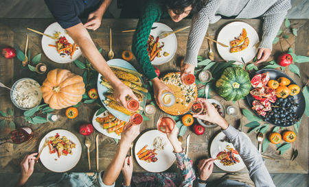 Vegan or vegetarian Thanksgiving, Friendsgiving holiday celebration. Flat-lay of friends eating and clinking glasses at Thanksgiving Day table with pumpkin pie, vegetables, fruit and wine, top view