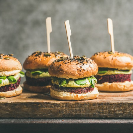 Flat-lay of healthy vegan burgers with quinoa beetroot patties, avocado cream and green sprouts on wooden board, grey wall at background, square crop. Vegetarian, clean eating, alkiline diet foodの写真素材