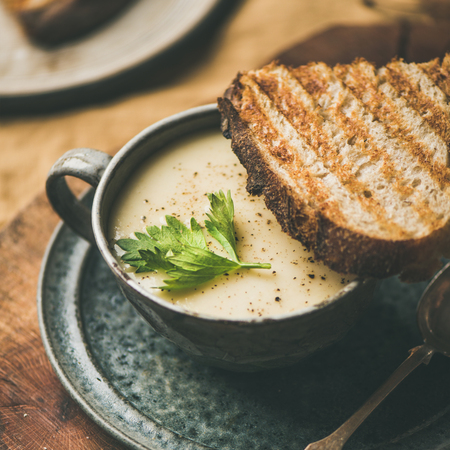 Autumn, Winter home dinner. Fall warming celery cream soup in cup and toast over yellow linen tablecloth, close-up, square crop. Comfort food, vegan, vegetarian, healthy and slow food conceptの写真素材