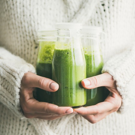Winter seasonal smoothie drink detox. Female in light knitted sweater holding bottles of green smoothie or juice in her hands, square rop. Clean eating, weight loss, healthy dieting food conceptの写真素材