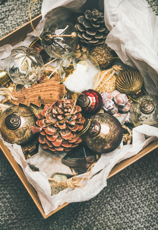 Christmas or New Year preparations. Flat-lay of various vintage Christmas tree decoration toys and pine cones in wooden box over grey floor background, top view. Festive holiday moodの写真素材