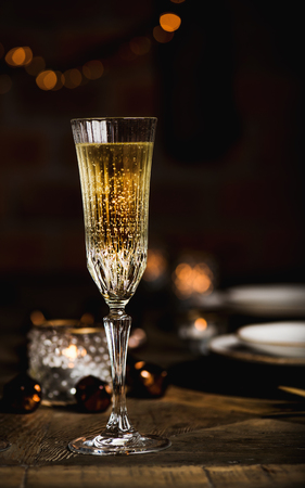 Christmas, New Year festive set, table with glasses of champagne, dinnerware, candles, decoration toys, wreath, sparkling garland, brick wall behind, copy space. Holiday celebration, New Year nightの写真素材