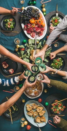 Company of friends gathering for Christmas or New Year party dinner at festive table. Flat-lay of hands holding glasses with drinks, feasting and celebrating holiday, top view, vertical compositionの写真素材