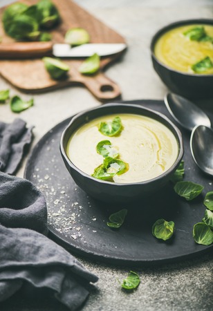 Seasonal brussels sprouts vegetable cream soup in black bowl and fresh green brussel sprouts over grey concrete background, vertical composition. Vegan, vegetarian, healthy, dieting food conceptの写真素材