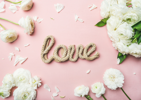 Saint Valentines Day background. Flat-lay of white ranunculus flowers and word love over light pink background, top view. Greeting card or wedding invitationの写真素材