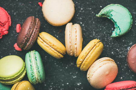 Sweet colorful French macaroon cookies variety with sugar powder over black background, top view, selective focus, close-upの写真素材