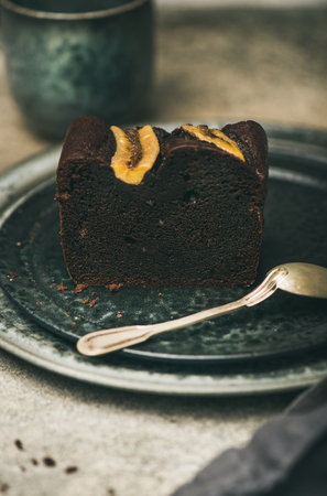 Piece of freshly baked dark chocolate banana bread cake dessert on grey plate over concrete tableの写真素材