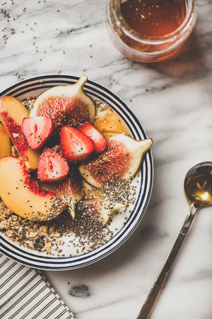 Healthy summer breakfast set. Flat-lay of Greek yogurt granola bowl with strawberry, figs, peach, chia seeds and honey over marble background, top view. Vegetarian, dieting, detox food conceptの写真素材