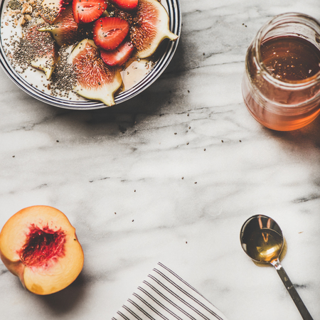 Healthy breakfast. Flat-lay of Greek yogurt granola bowl with strawberry, figs, peach, chia seeds and honey over marbleの写真素材