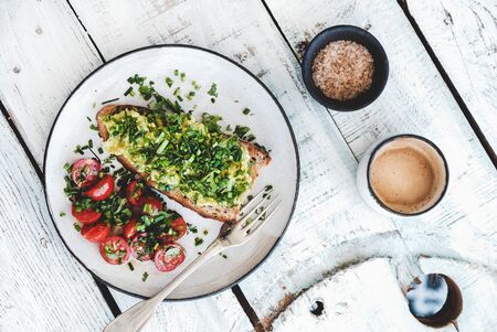 Healthy vegan lunch. Flat-lay of avocado toast on sourdough bread with chives, coriander, cherry-tomatoes with cup of coffee over whiteの写真素材