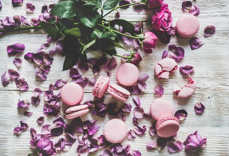 Sweet pink macaron cookies and spring rose flowers, buds and petals over wooden tableの写真素材
