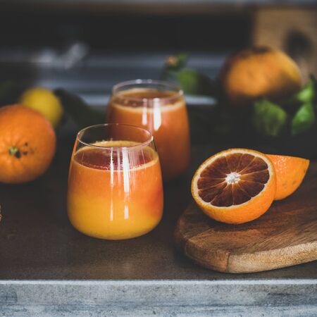Glasses of freshly squeezed blood orange juice or smoothie on concrete kitchen counter, square crop, close-up.の写真素材