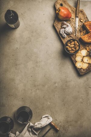 Wine and snack set. Flat-lay of wine bottle, two glasses of red wine, vintage corkscrews, cheese and appetizers on wooden board over dusty concreteの写真素材