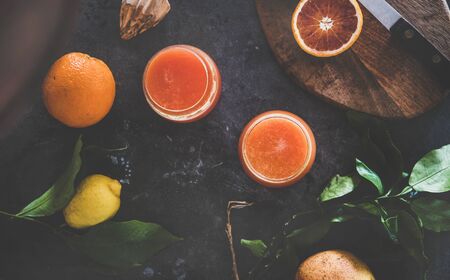 Flat-lay of two glasses of freshly squeezed blood orange juice or smoothie and fresh fruits over blackの写真素材