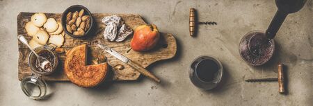 Wine and snack set. Flat-lay of two glasses of red wine, vintage corkscrews, cheese and appetizers on board over concreteの写真素材