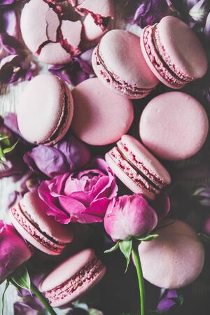 Sweet pink macaroon cookies and spring rose flowers, buds and petals over woodenの写真素材