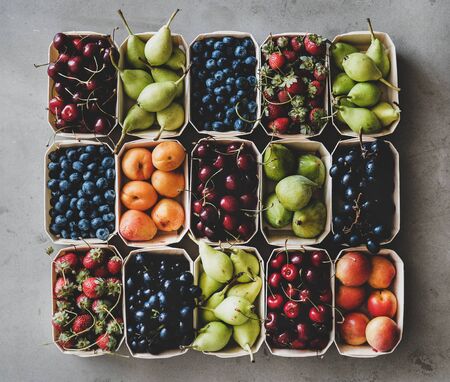 Summer fruit and berry variety. Flat-lay of strawberries, cherries, grapes, blueberries, pears, apricots, figs in wooden eco-friendly boxes over grey background, top view. Local farmers produceの写真素材