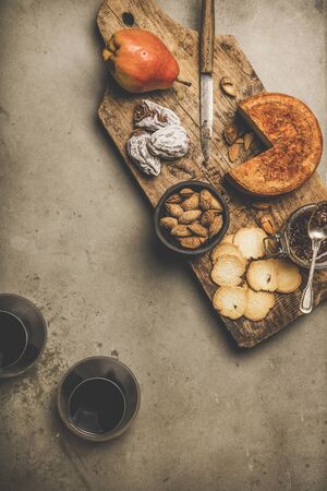 Wine and snack set. Flat-lay of two glasses of red wine, vintage corkscrews, cheese and appetizers on wooden board over dusty concrete background, top view, copy space. Party food conceptの写真素材