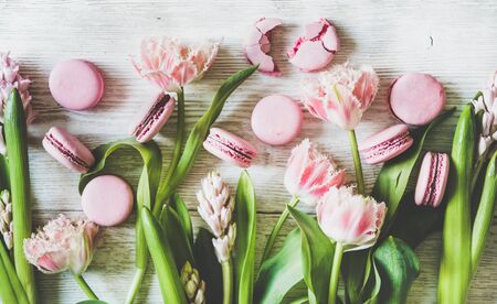 Flat-lay of sweet pink macaron cookies and fresh spring flowers over white wooden background, top view. Food texture, background and wallpaperの写真素材
