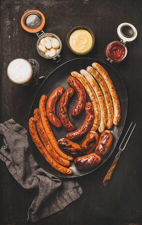 Flat-lay of Octoberfest party dinner table concept with grilled veal and pork sausages, sauce, pickled vaggies and beer in glass over dark background, top viewの写真素材