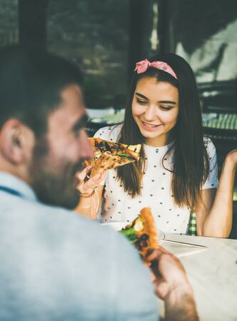 Young happy caucasian couple sitting at table eating pizza in Italian cuisine cafe on sunny summer dayの写真素材