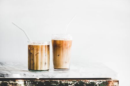 Homemade iced latte coffee in glasses with straws on grey marble table, white wall at background, copy space. Summer cold refreshing drink conceptの写真素材