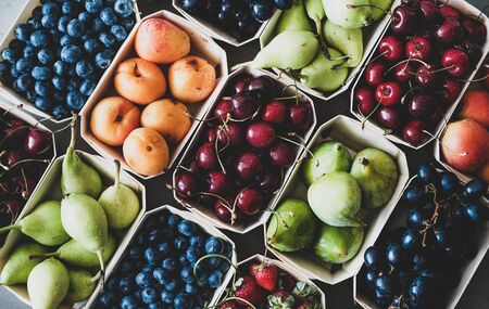 Summer fruit and berry variety. Flat-lay of ripe strawberries, cherries, grapes, blueberries, pears, apricots, figs in wooden eco-friendly boxes over grey background, top view. Local farmers produceの写真素材