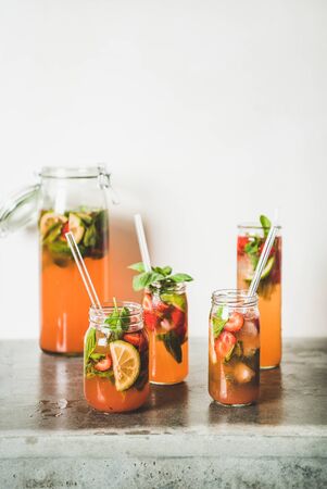 Homemade strawberry and basil lemonade or ice tea in glass tumblers with eco-friendly plastic-free straws on grey concrete table, white wall at background, copy space. Summer refreshing soft drinkの写真素材
