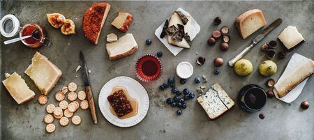 Wine snack variety. Flat-lay of cheeses, honey, fruit, nuts, crackers and wine in glass over rough grey concrete background, top view. Gathering, party, holiday food conceptの写真素材